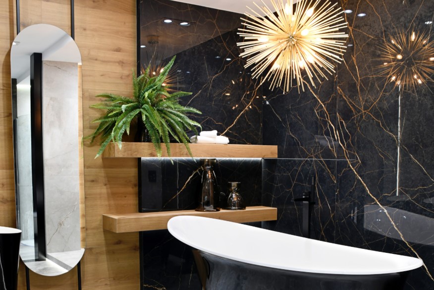Ciemna łazienka z płytkami drewnopodobnymi i imitacją czarnego marmuru ze złotą nitką i wanną wolnostojącą