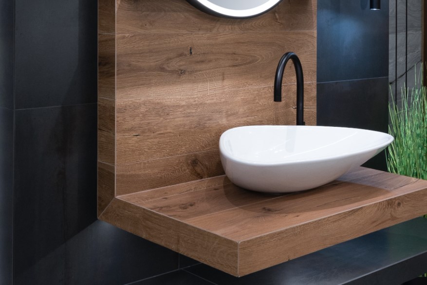 Czarne matowe płytki w łazience z nowoczesnym blatem z płytek drewnopodobnych i wolnostojącą umywalką
