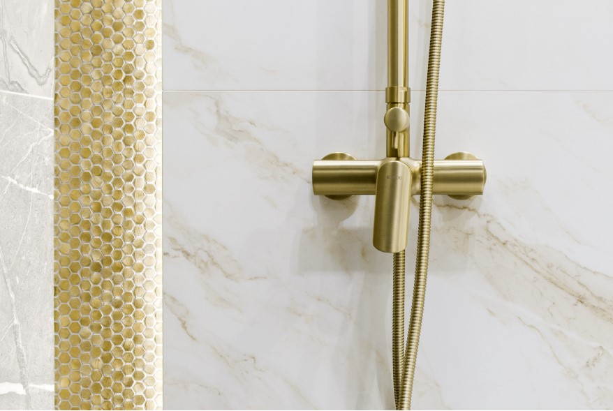 Białe płytki w imitacji marmuru ze złotym dekorem i złotą baterią prysznicową