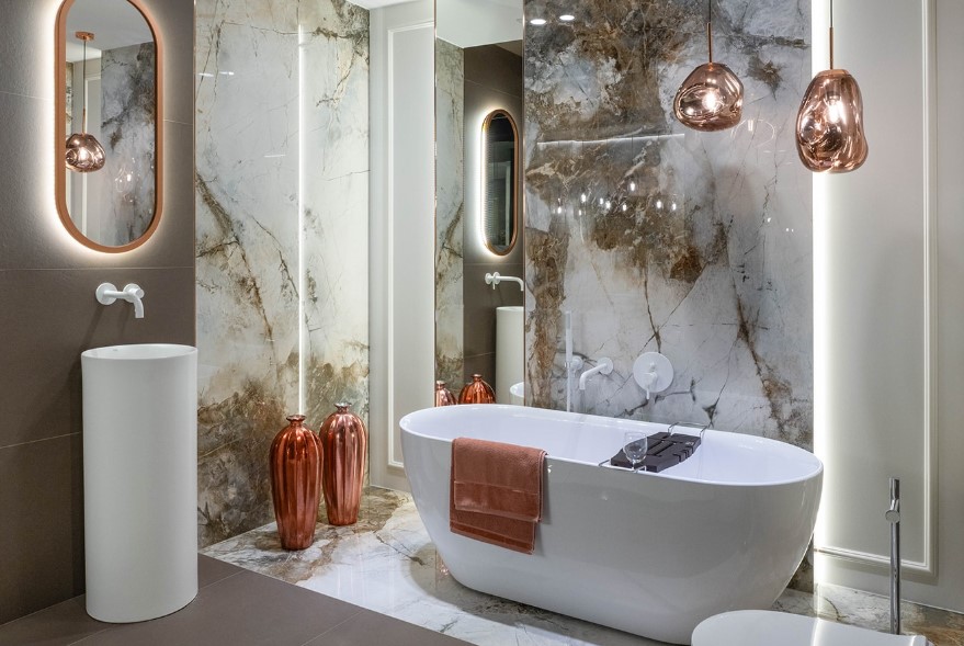 Biała wanna wolnostojąca w aranżacji w odcieniach beżu i miedzi.