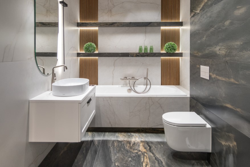 Łazienka w odcieniach bieli i szarości z wanną zabudowaną płytkami z imitacją marmuru.